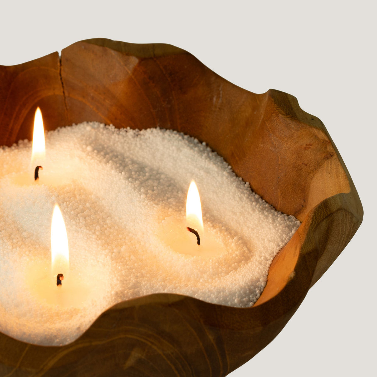 Close detail of white unfragranced candle sand lit with three wicks in a wooden bowl