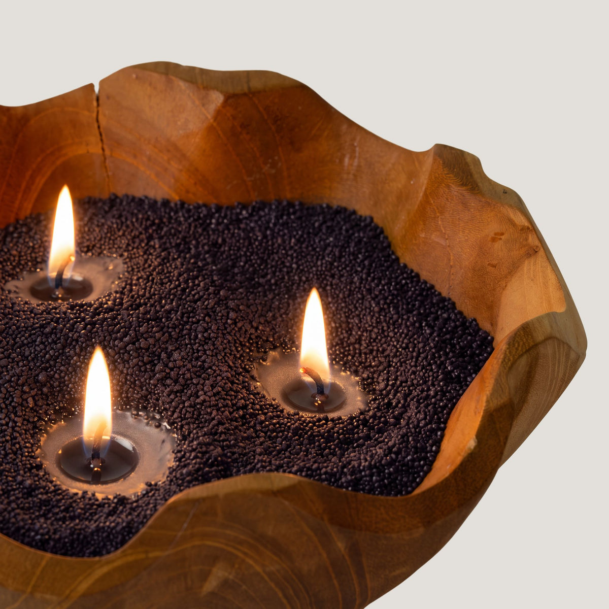 Close detail of black Spirited candle sand lit with three wicks in a wooden bowl